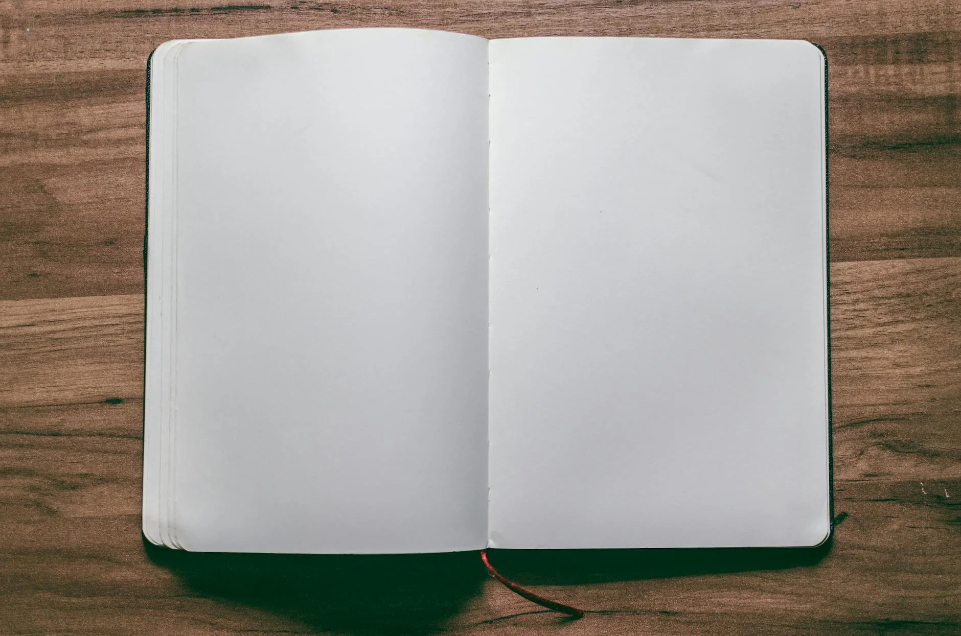 A top-down view of an open blank notebook on a wooden desk, perfect for design or writing projects.
