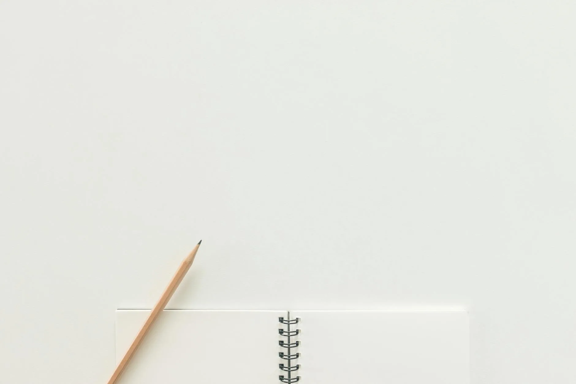 A top view of a spiral notebook with pencil on a neutral light background, ideal for creative workspaces.