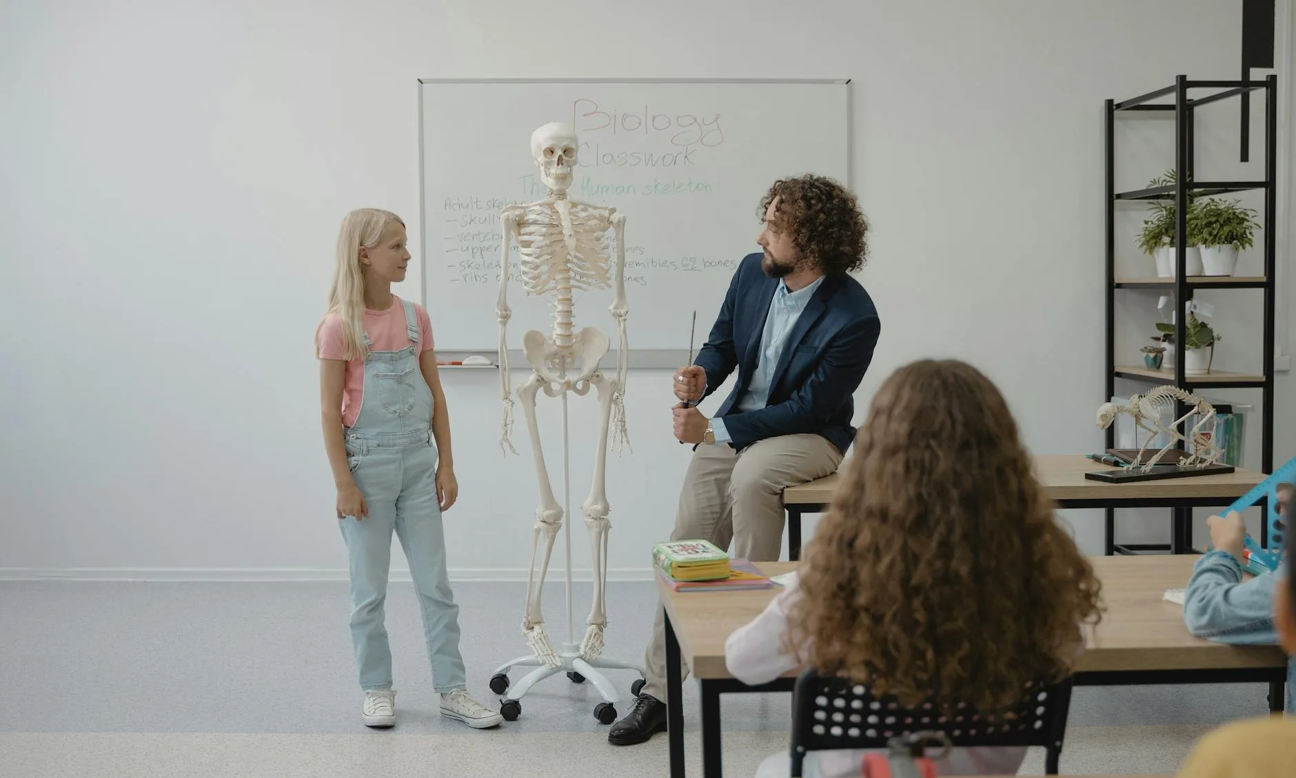 Teacher and students in a classroom using a skeleton model for a biology lesson.