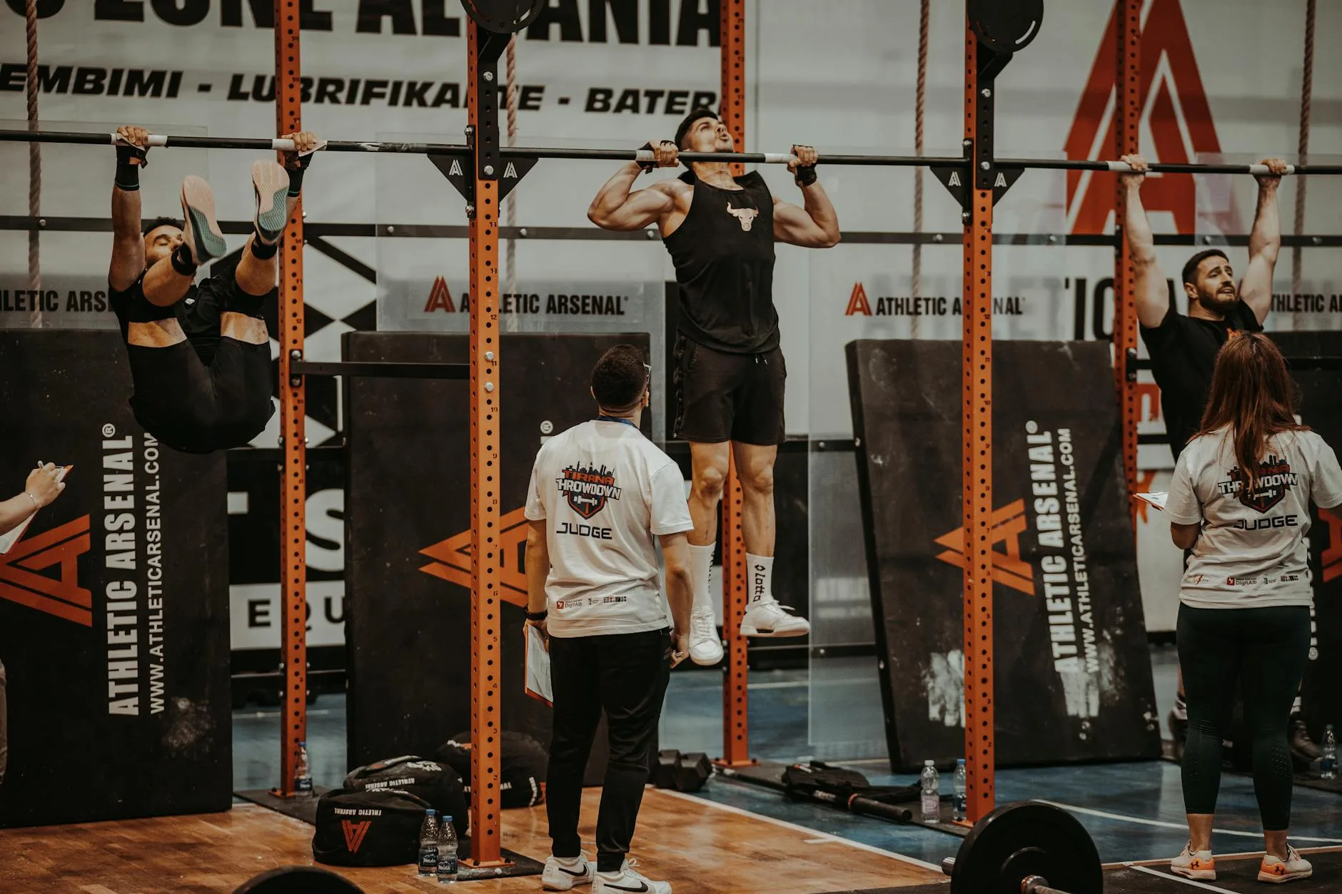 Athletes performing pull-ups in a CrossFit competition, judged by officials, showcasing strength and endurance.